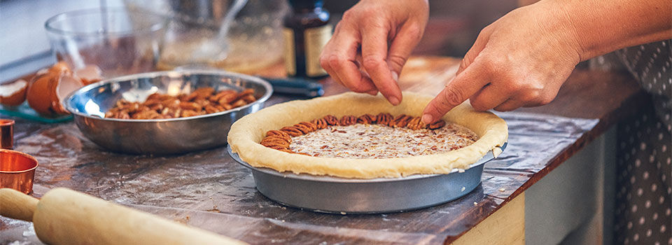 Woman in the kitchen putting pecans on a pie before putting it in the over to bake