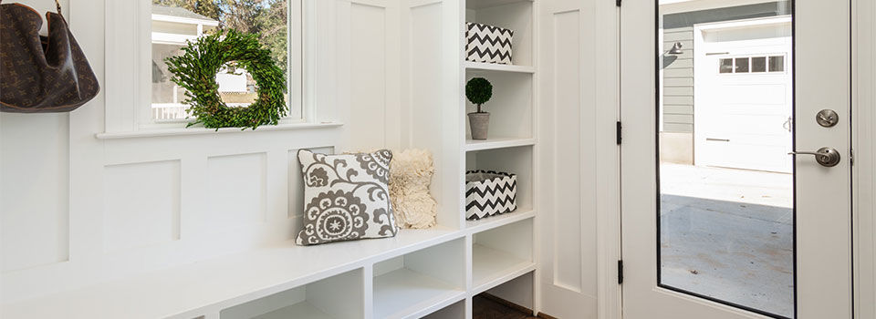A modern styled mudroom with a glass door and white shelving used to store jackets, boots and shoes