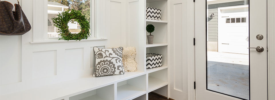 A modern styled mudroom with a glass door and white shelving used to store jackets, boots and shoes