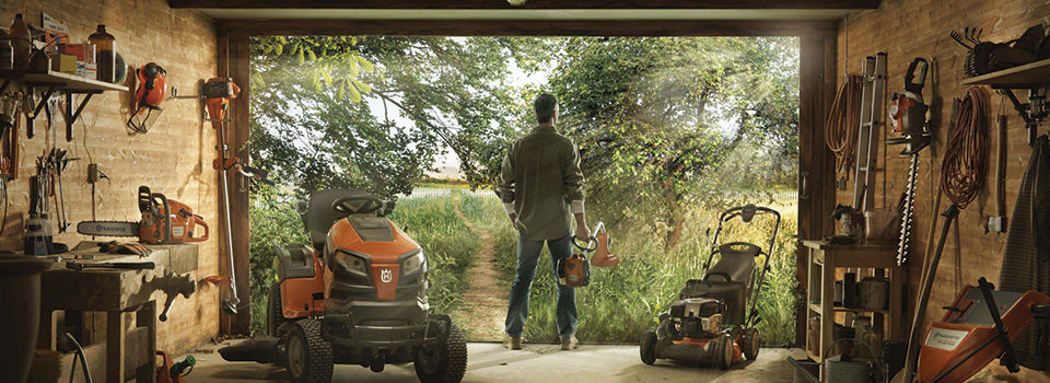 Man standing in garage full of lawn tools looking out at an overgrown yard