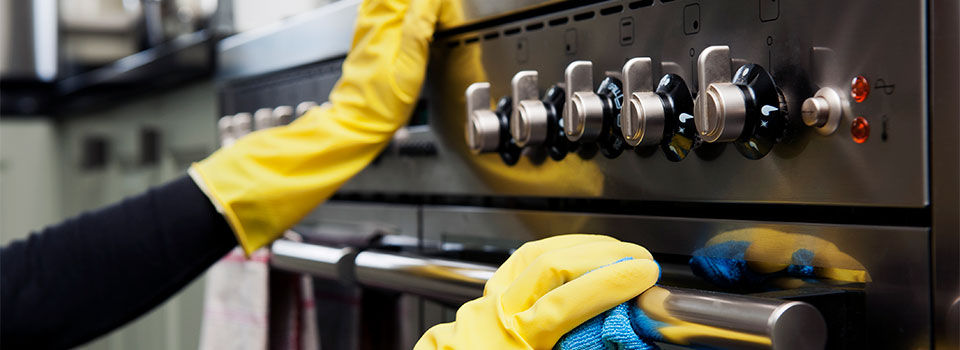 Person cleaning the front of their oven wearing yellow rubber cleaning gloves using a microfiber cloth