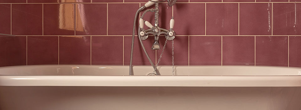 A ceramic bathtub with pink tile on the wall