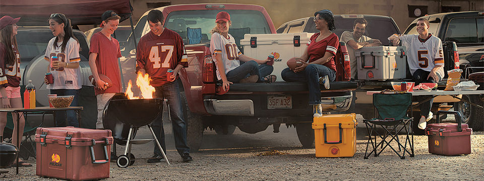 A group of young adults tailgating for a football game and using Pelican coolers to keep the beverages cold