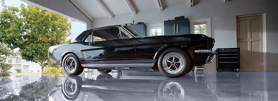 A black old school hot rod sitting in a garage on a sleek silver garage floor