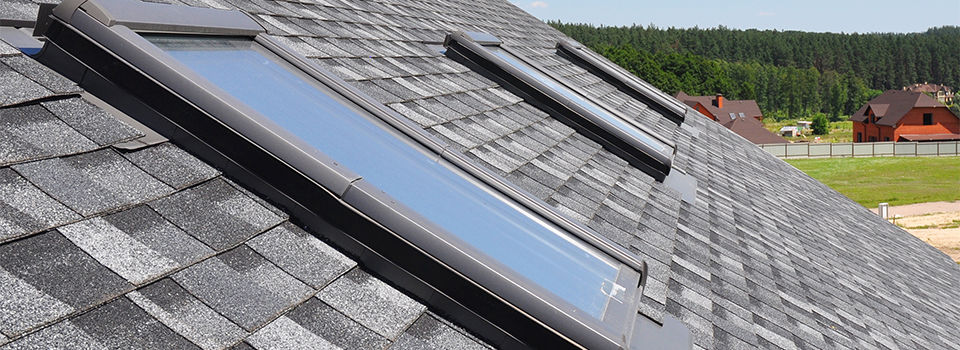A slate gray shingle roof with three skylights lined up in a row