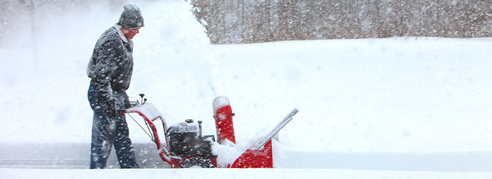 A man using a red gas powered snow blower to clear his driveway of snow