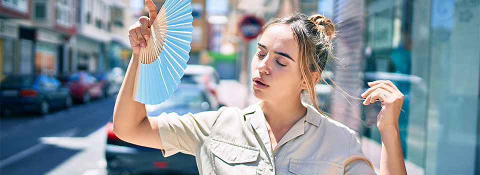 Young beautiful blonde caucasian woman smiling happy outdoors on a sunny day using handfan for hot weather