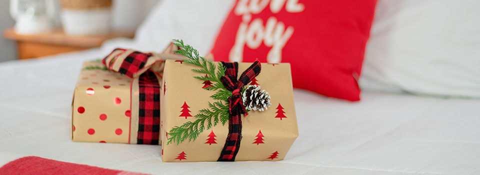 Two wrapped Christmas gifts with bows sitting on a bed