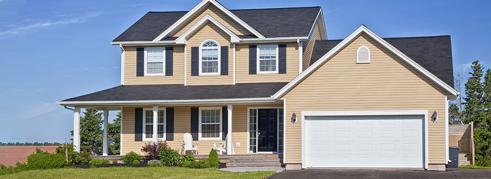 A residential two story home with tan vinyl siding and slate gray shingle roofing