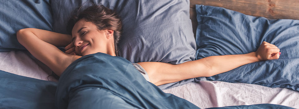 A young woman laying in her bed stretching her arms as she wakes up for the day