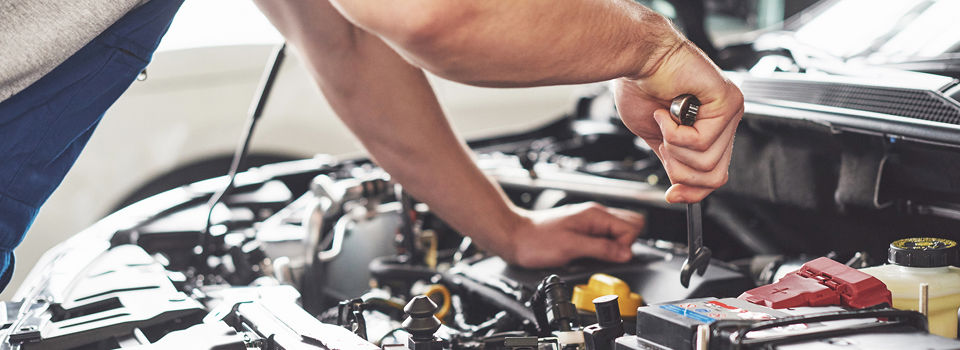 30-something man leaning over car engine while holding a wrench.