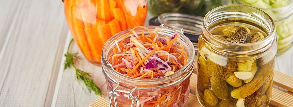 Fermented preserved vegetarian food concept. Sour sauerkraut, pickled carrots, pickled cucumbers, pickled celery in glass jars on a white wooden kitchen table. The concept of canned food.