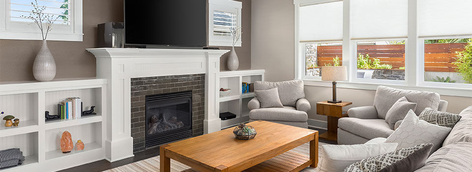 A modern living room with white shelving units around a brick fireplace and white mantel. There is a wooden coffee table surrounded by gray chairs and a gray couch