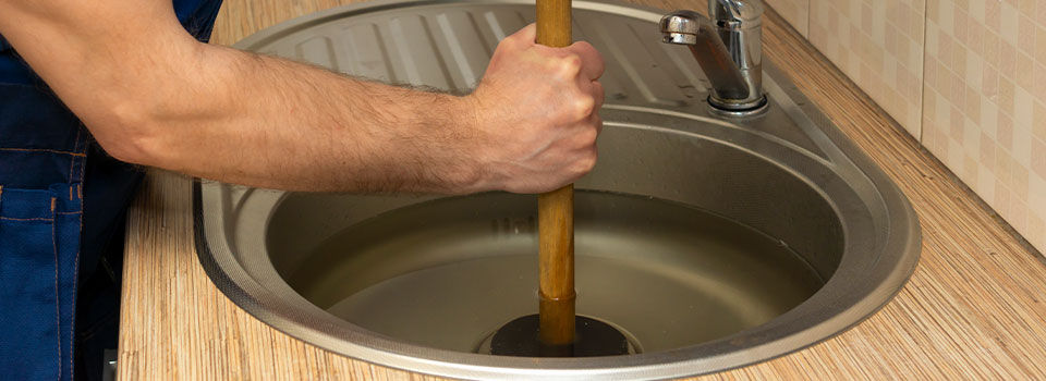 Person trying to unclog a sink with a plunger