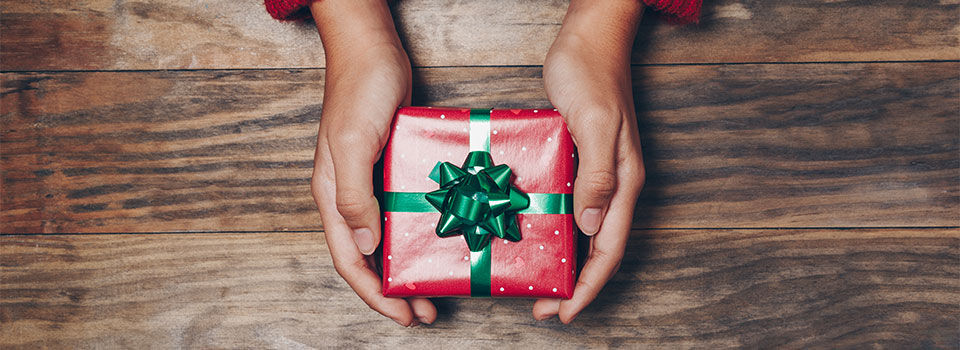 Person holding a small wrapped gift in their hands over a wood background