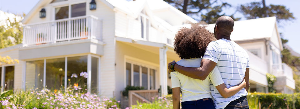 Weekend fun at home together. Rear view of a mixed race couple standing in the garden, embracing and looking at the house