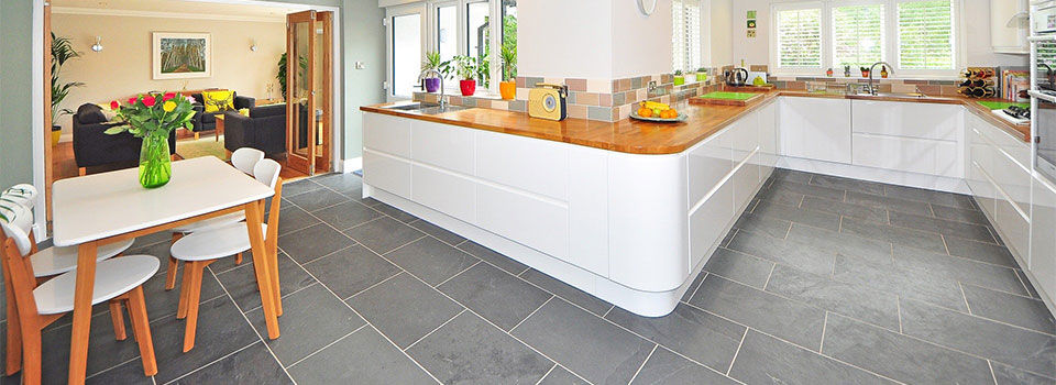 A kitchen with grey tile throughout with white cabinets and wood countertops