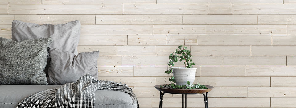 White decorative shiplap haning on a bedroom wall. The bed has gray sheets with a small side table and plant.