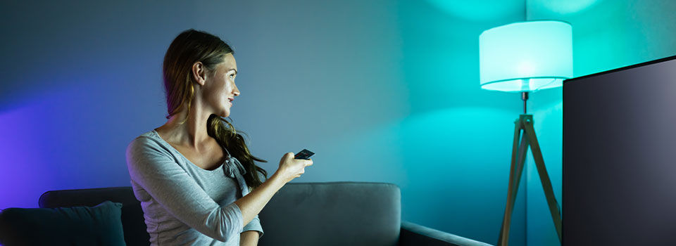 Woman sitting on couch and turning her colored lamp on with a remote