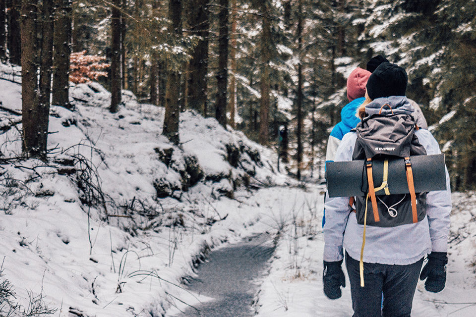 A couple walking out in the winter woods. They are wearing winter coats, gloves, hats and carring hiking bags. 