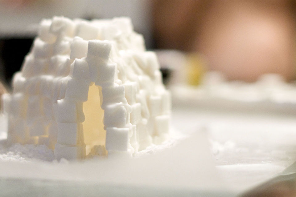 a childs indoor craft project of an sugar cube igloo. The igloo is sitting on top of parchment paper on the kitchen counter. 