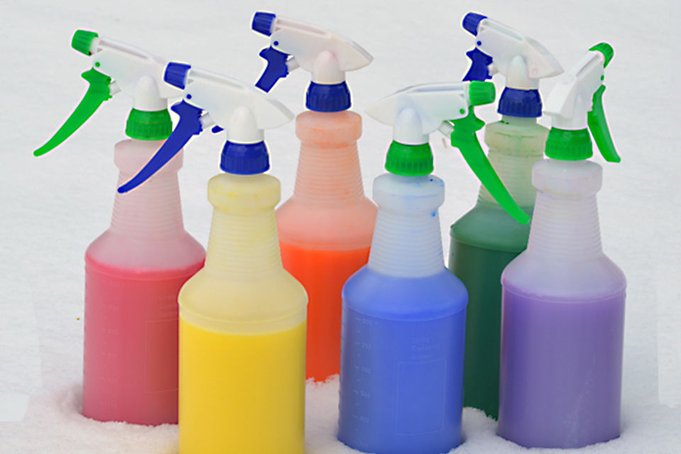 Colored paint in spray bottles. The bottles are sitting out side in a snowy yard. There are six different colors