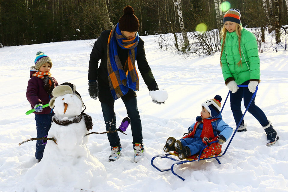 a family of four building a snowman out in a winter wonderland. 