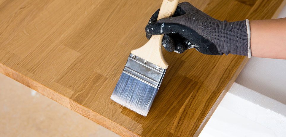 Person wearing a latex glove staining a piece of wood with a paint brush
