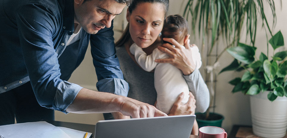 Wife holds baby close to her while husband is pointing at computer screen