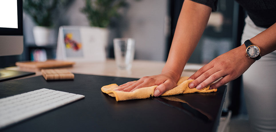 Person wiping down their workspace with an orange microfiber towel