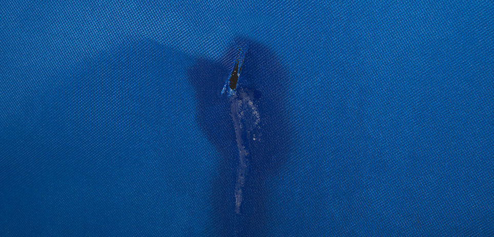 A blue piece of vinyl pool lining is darker around a tear, showing where there’s a leak in the pool.