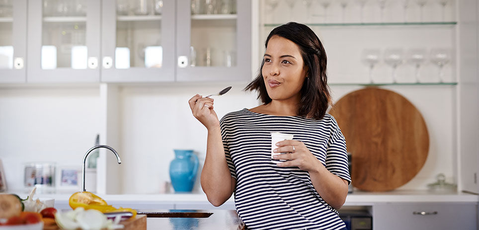 Woman leaning against kitchen countertop while enjoying a cup of yogurt