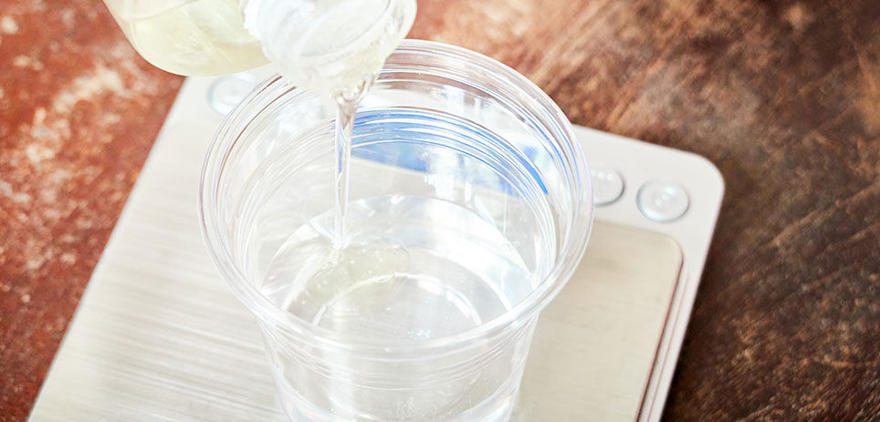 Pouring an epoxy mixture into a plastic cup on a small scale to weigh