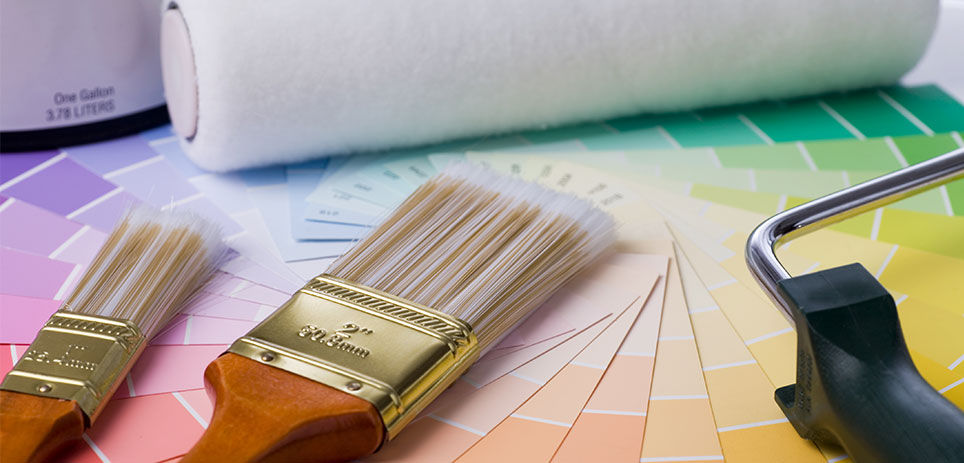 Close-up of professional painting supplies including various paint brushes, a roller, a paint can, and colorful paint samples. Ideal for DIY projects or professional use. High-quality materials guarantee a smooth and even application. 