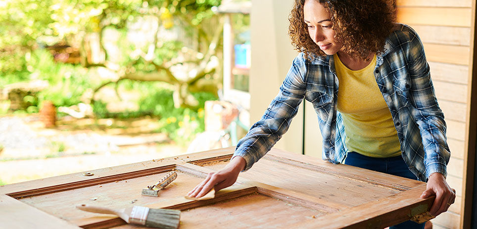 A skilled woman restores a vintage wooden door through the process of sanding. She carefully sands the surface of the door, highlighting its natural wood grain and bringing it back to life.