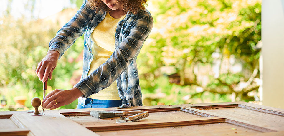 An experienced woman prepares to sand a vintage wooden door by removing its handle.