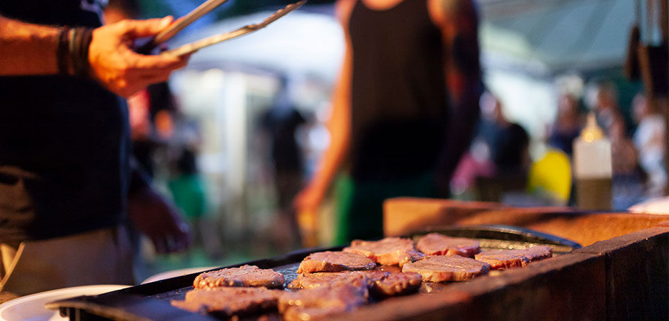 Man holding tongs while grilling burgers