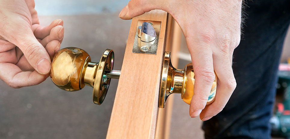 Door installation, worker Installs door knob, woodworker hands close-up.