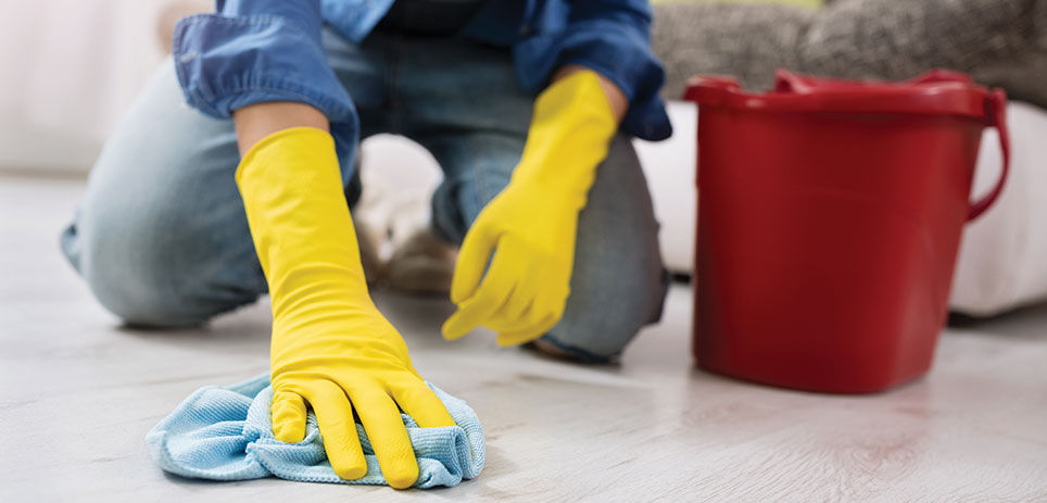 Person on the ground with a rag cleaning the floor with a red bucket beside them