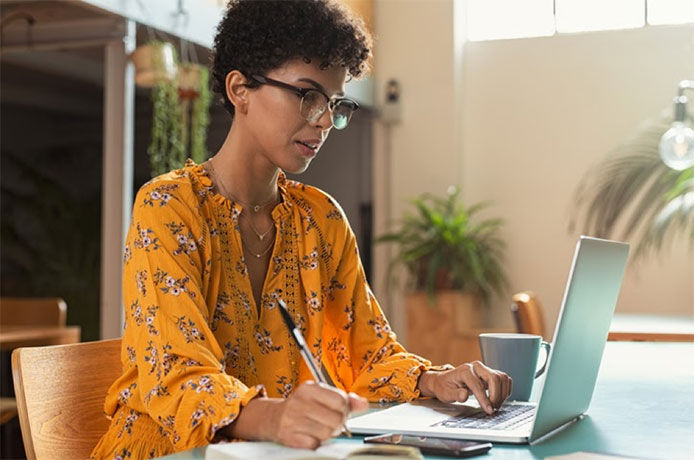 Woman with glasses working on her laptop taking notes