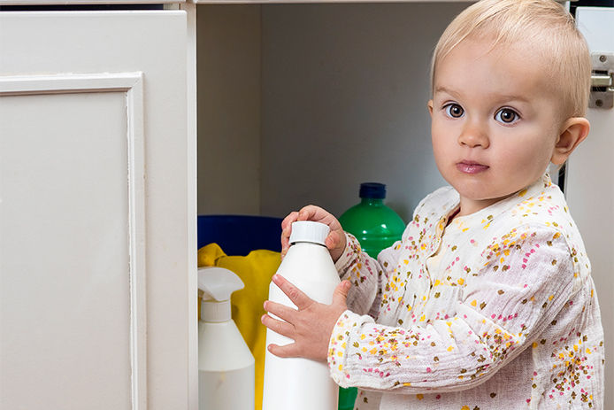 Young baby girl exploring the cleaning cabinet under the sink, a potentially dangerous area for young children. This image serves as a reminder to secure all potentially hazardous household items and keep them out of reach of curious children.