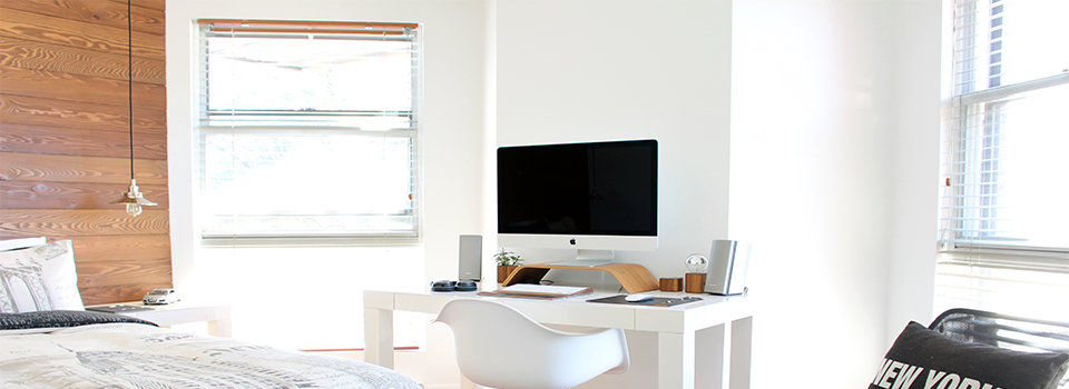 A bedroom/office space with white blinds on thw windows