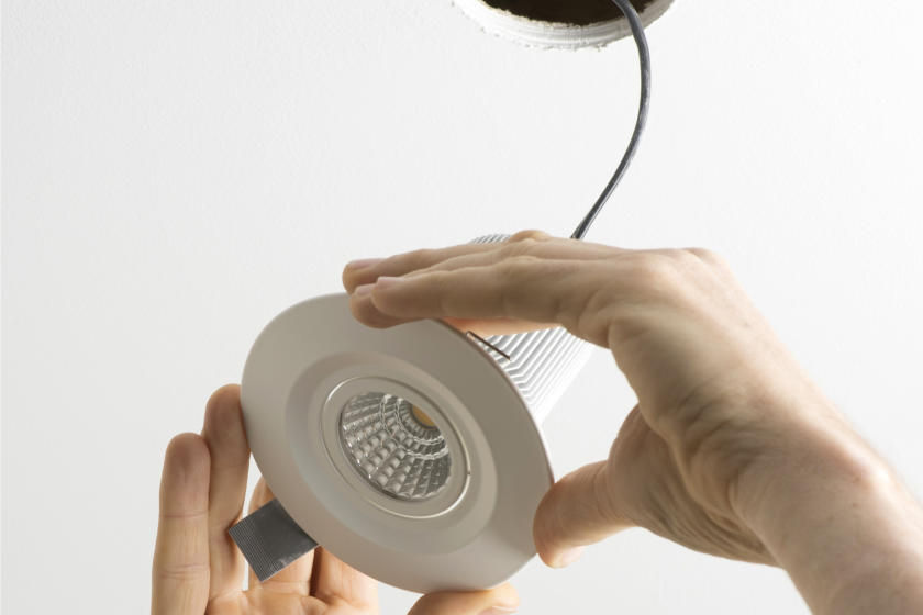 Hands holding flush-mount light fixture hanging by its wires from the ceiling