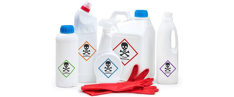 Five white plastic chemical bottles with chemical warning labels and a pair of red rubber gloves, isolated on a solid white background. These chemical bottles are labeled with various hazardous chemical warnings and contain industrial-strength cleaning solutions. The red rubber gloves are protective gear used to handle these chemicals safely. Ideal for use in industrial, manufacturing, or laboratory environments.