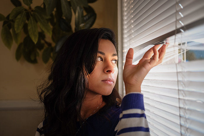 A woman peeking outside through her blinds