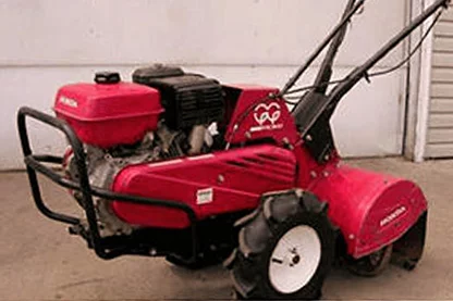 A red garden tiller in front of a house garage door